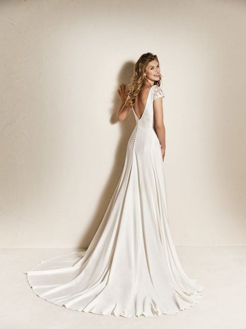 The simplicity of the crepe is what gives form and life to this spectacular flared wedding dress with cap sleeves in lace. A beautiful design that combines a fitted bodice featuring a V-neck in the front and back with a luxurious skirt and long train. A wedding dress with beaded appliqués on the sleeves that tiny sparkles to the final look.