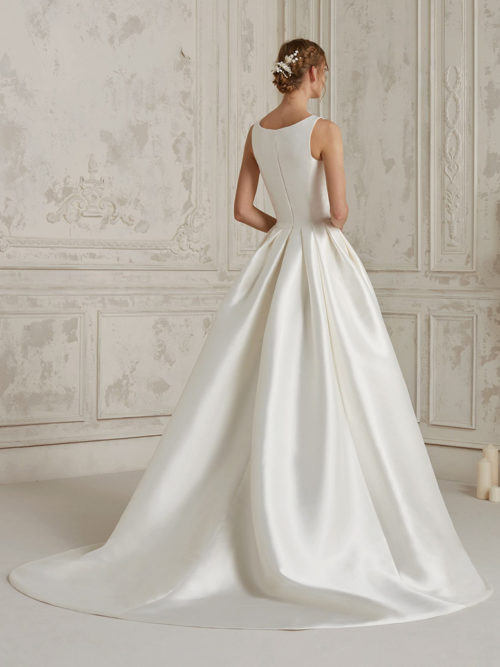 Elegant and ultra-sophisticated. A classic dress that uses femininity and the natural beauty of mikado to create this fabulous princess design with a natural waist and a subtle centre slit and a buttoned bodice with a jewel neckline and closed back.