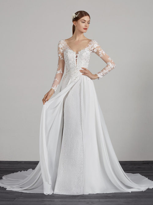 Romantic and very sensual. A dress with double skirt effect that combines a lace mermaid skirt with a chiffon overlay, open at the centre, with natural waist. Moreover, the close-fitting lace and tulle bodice enhances the v-neck and creates a tattoo effect on the long sleeves, at the shoulders and at the edges of the neckline.