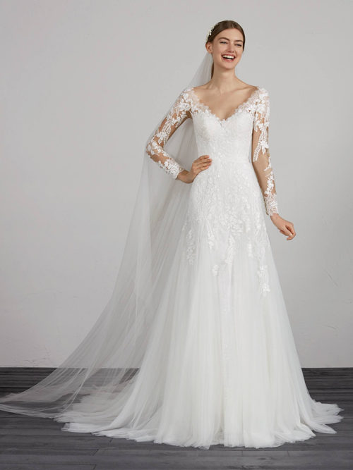 Sensational soft tulle evasé dress with lace appliqués both on the skirt with low waist and on the spectacular bodice framed by a modern v-neck with back and long sleeves crafted in tulle and lace with illusions