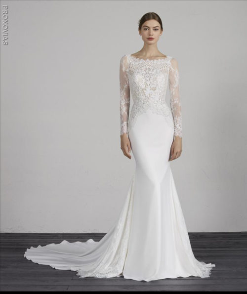 Lovely crepe mermaid dress with low waist and lace godets. A dress that creates a two-piece effect since it is combined with an illusion lace bodice and long sleeves, a flattering bateau neckline and v-back.